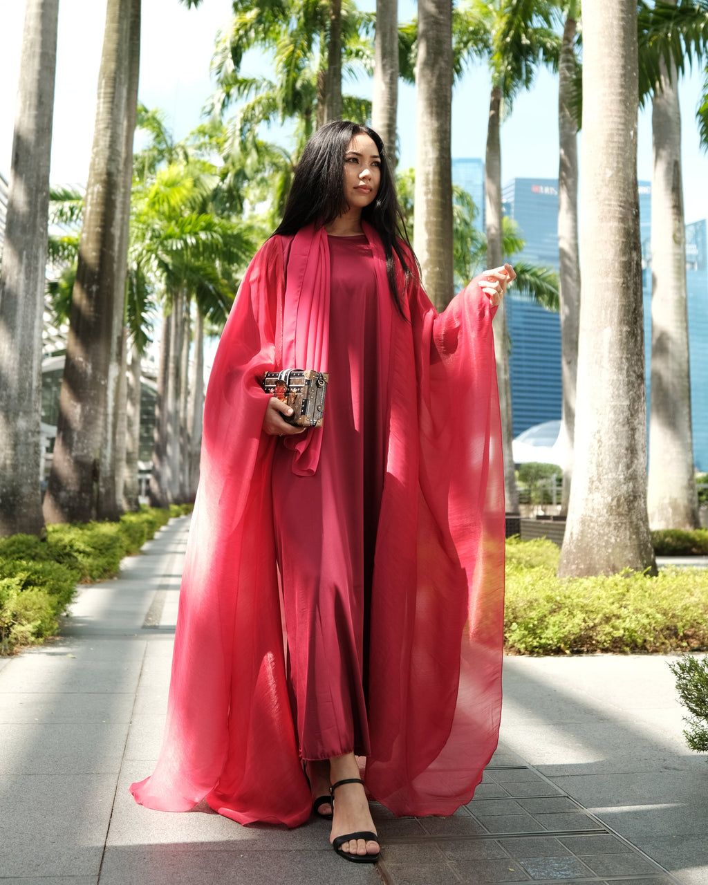 Woman in an  red abayas on a sidewalk with palm trees in the background