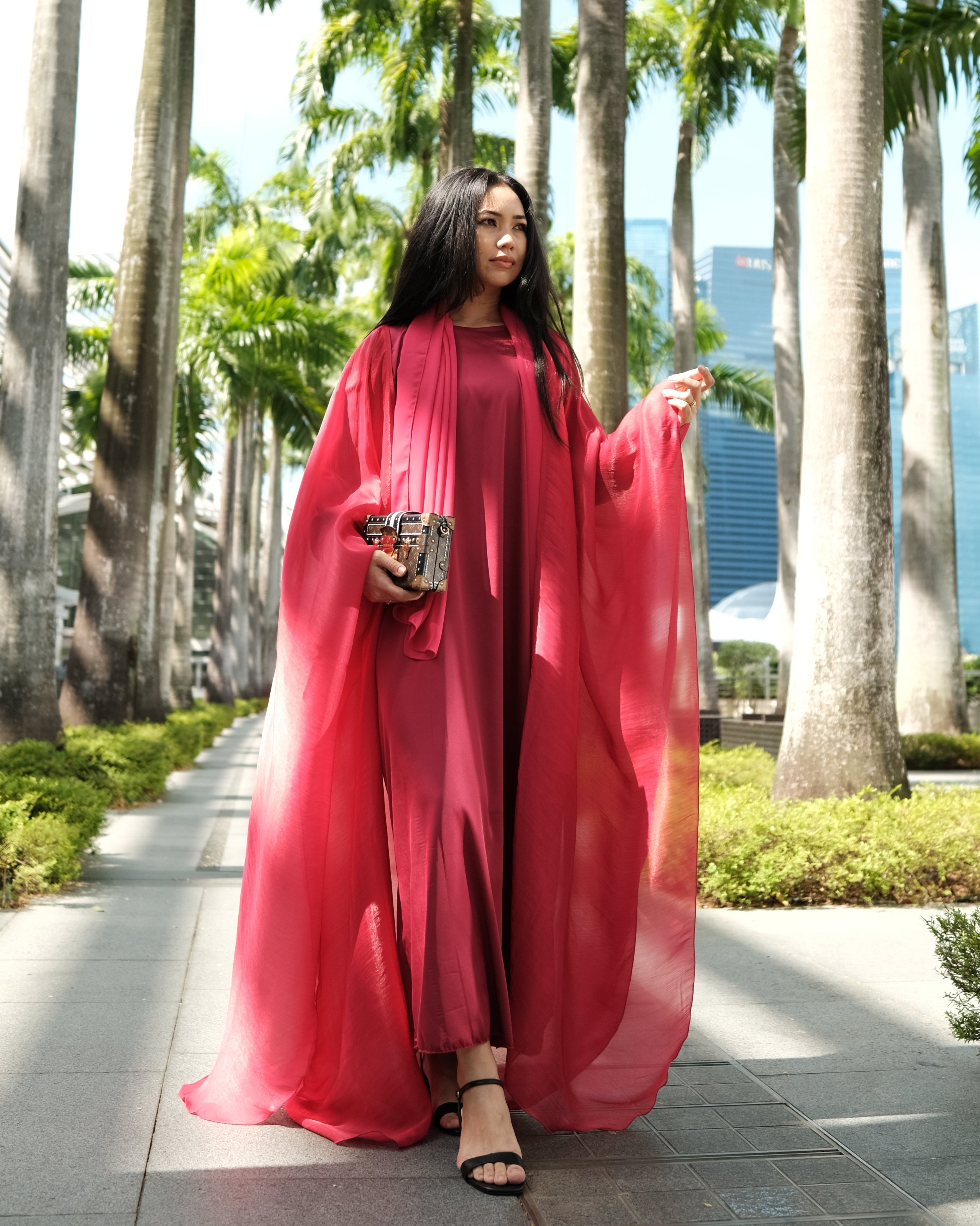 Woman in an  red abayas on a sidewalk with palm trees in the background